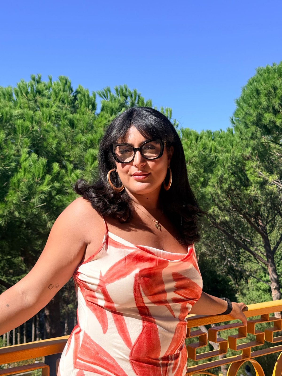 Jasmine Touitou en robe orange et crème, lunettes papillon, regard caméra
